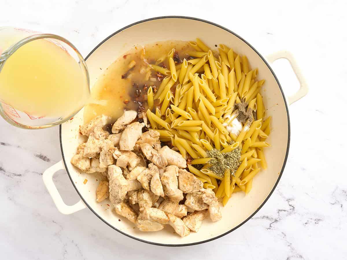Chicken, broth, and pasta added to a pot with sauteed onions.