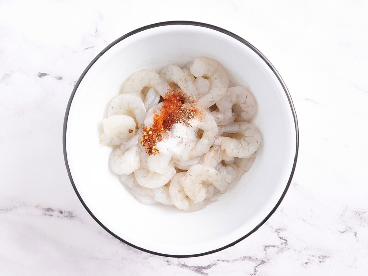 Defrosted shrimp in a bowl with seasoning.