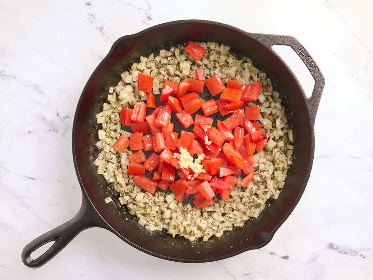Tomatoes added to a skillet with garlic and onions.