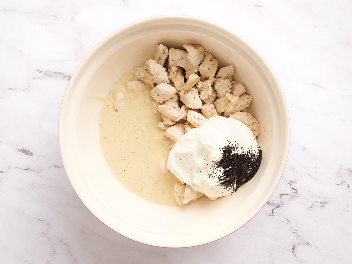 A mixing bowl with chicken, sour cream, poppy seeds, and sauce in a bowl.