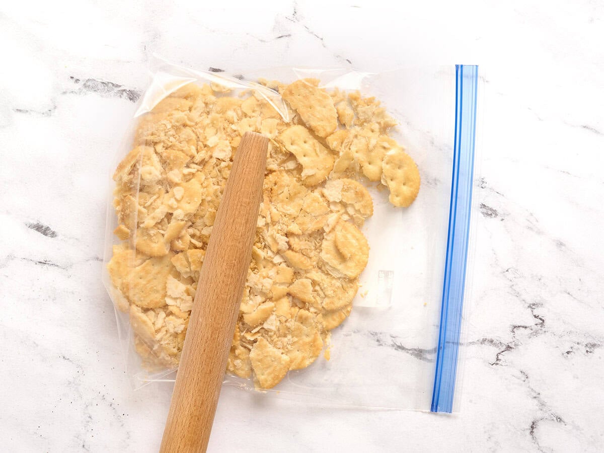 Crackers in a ziptop bag being crushed with a rolling pin.