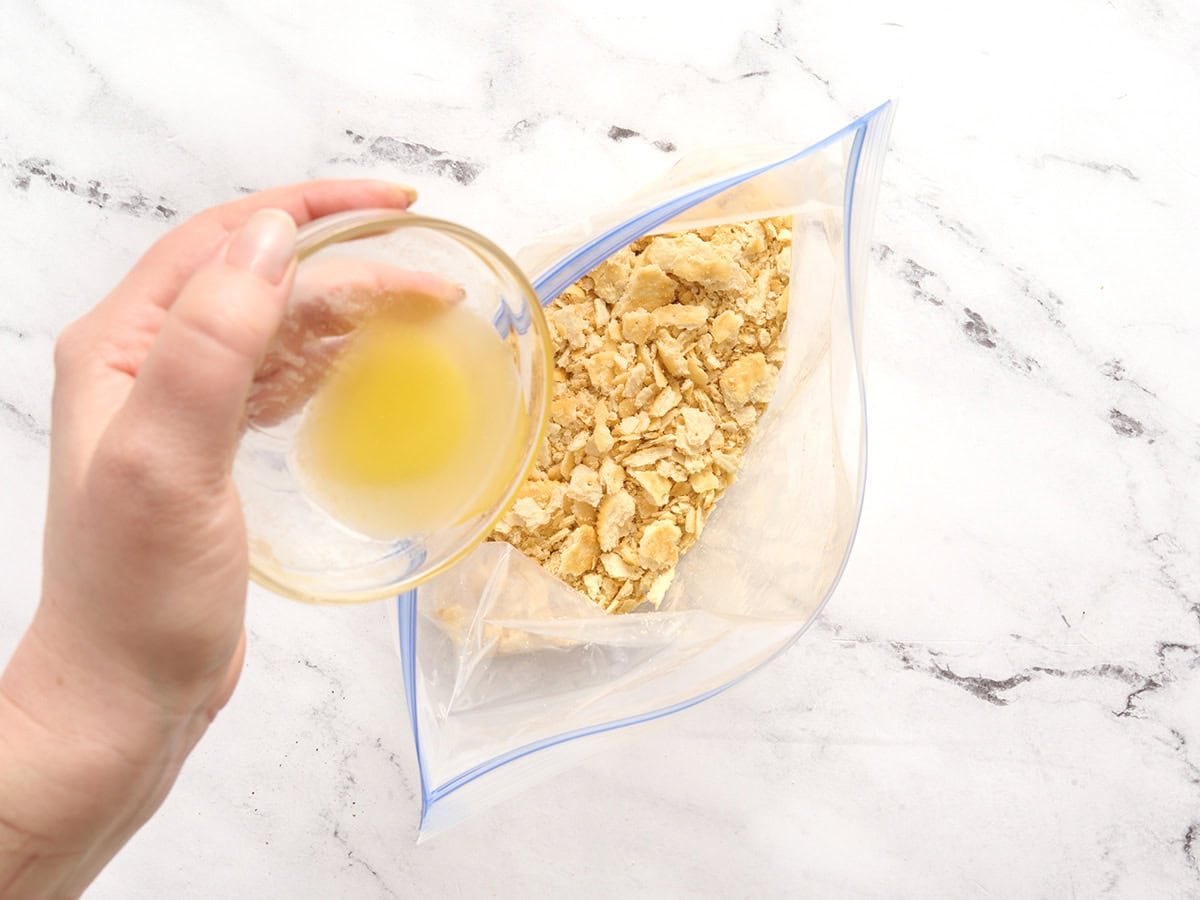 A ziptop bag of crushed crackers and melted butter being poured in.