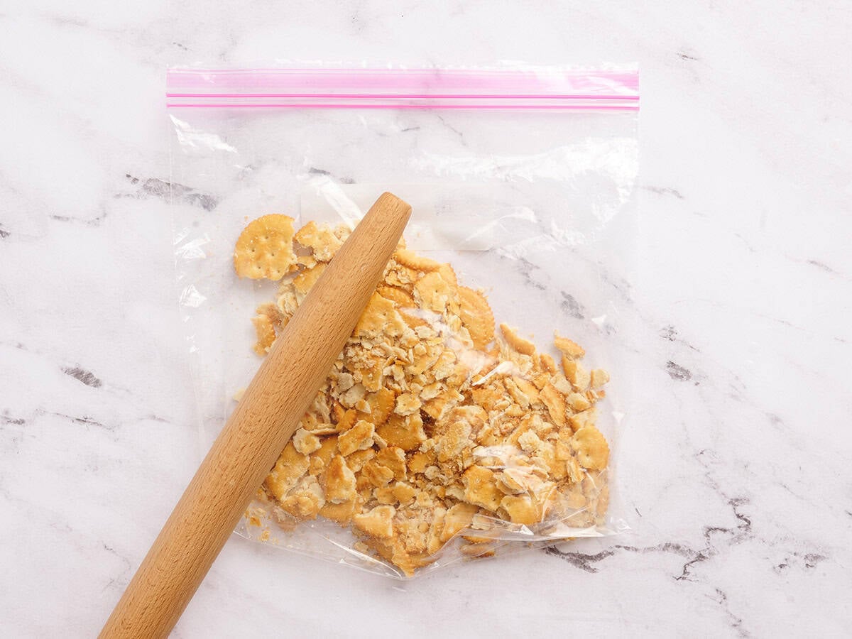 Crackers in a ziptop bag being crushed with a rolling pin.