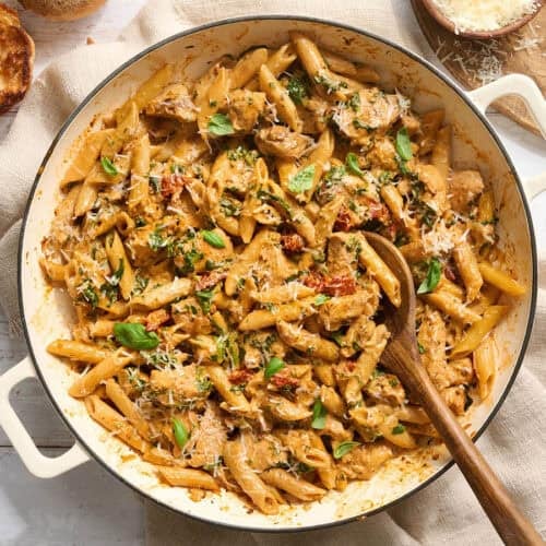 Overhead of marry me chicken pasta in a pot with a wooden spoon.