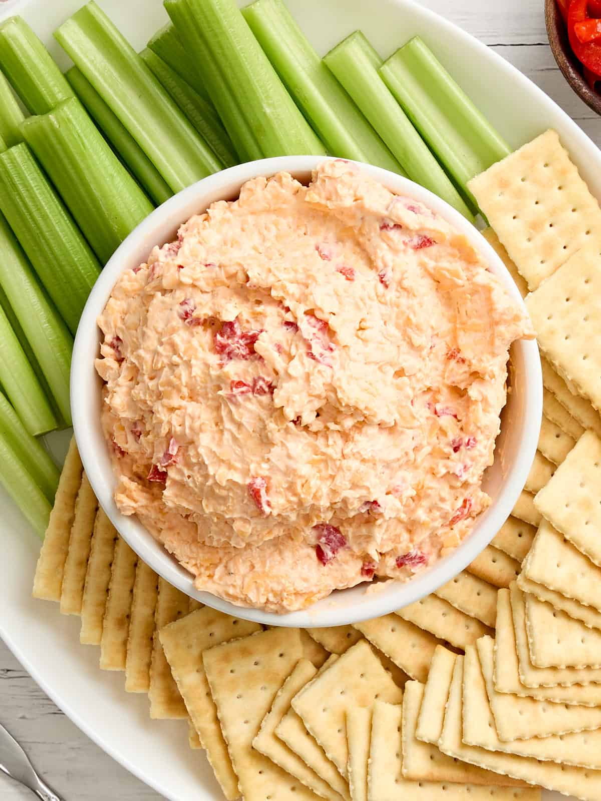 Overhead view of a bowl of pimento cheese with celery and crackers.