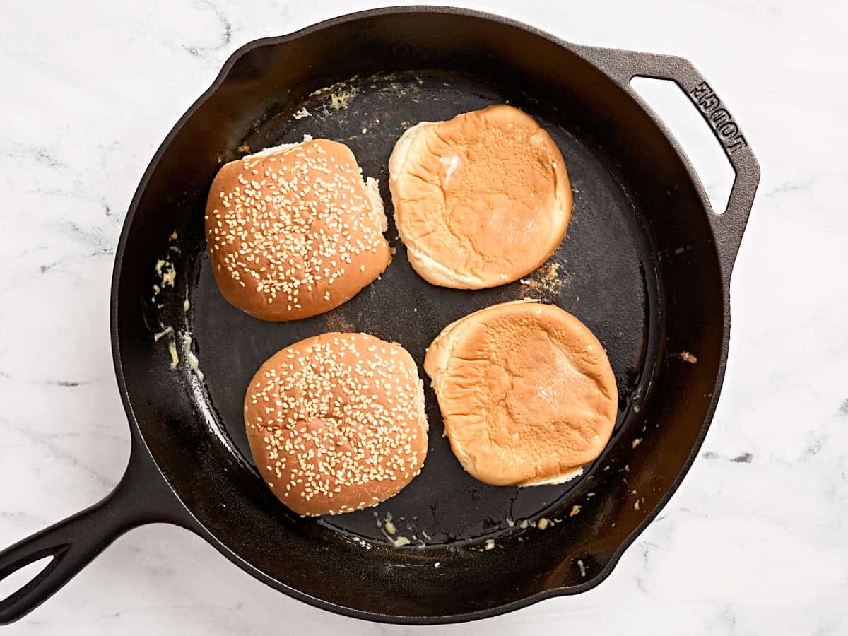 Burger buns toasting in a skillet.