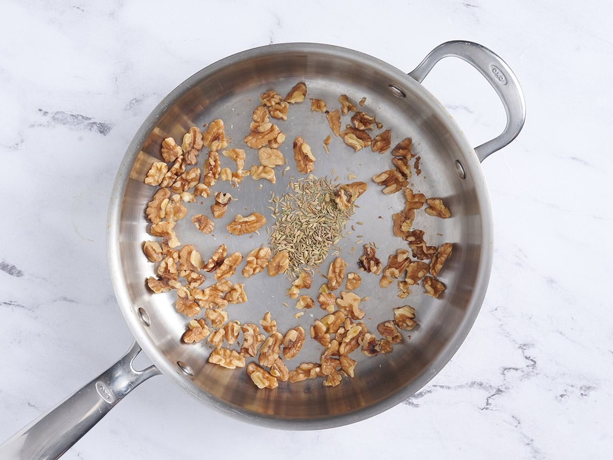 Fennel seeds and walnuts toasting in a skillet.