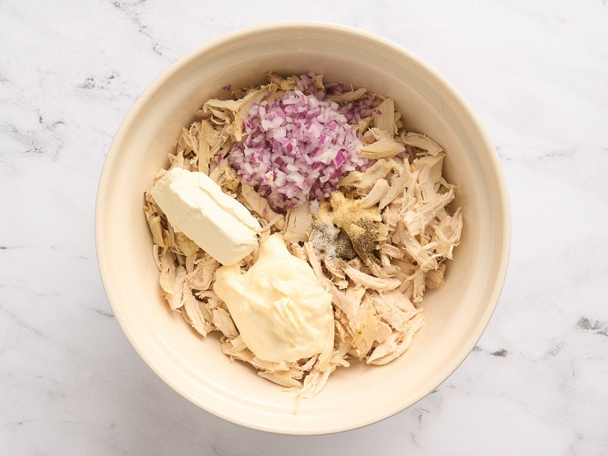 Shredded chicken, diced red onion, mayo, cream cheese and seasonings in a mixing bowl.