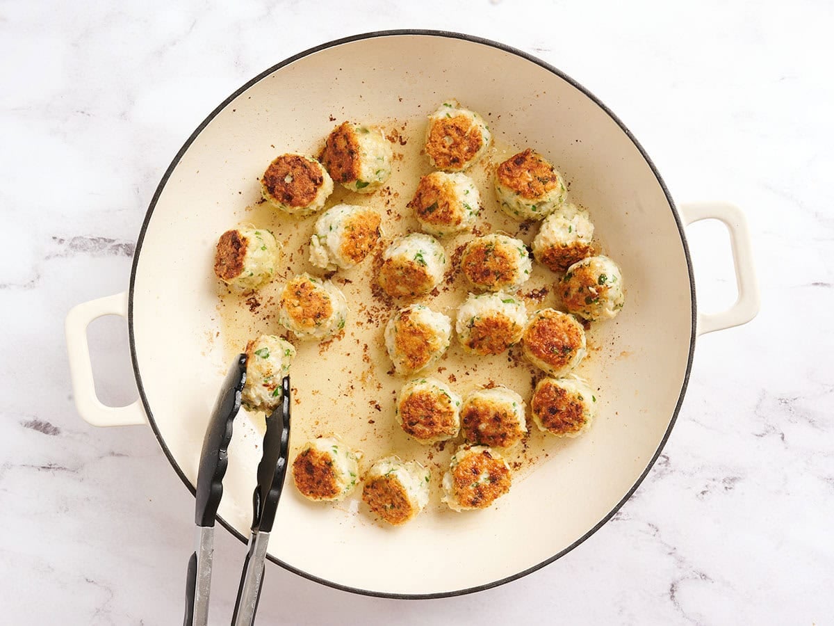 Chicken piccata meatballs in a skillet cooking.