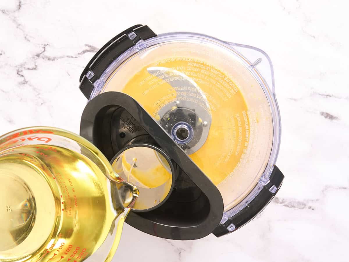 Oil being streamed into a food processor to make an emulsion for garlic aioli.
