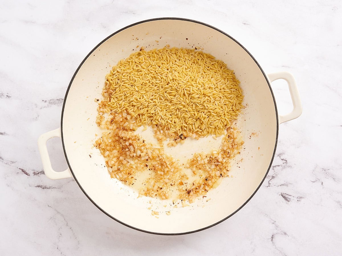 Dry orzo added to a skillet with onion and garlic.