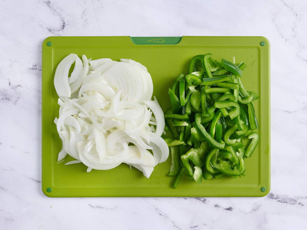 Sliced onions and green peppers on a cutting board.