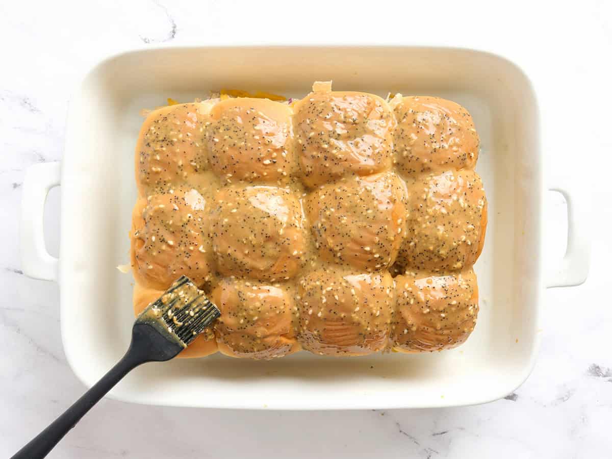 A pastry brush brushing chicken sliders with a butter topping.