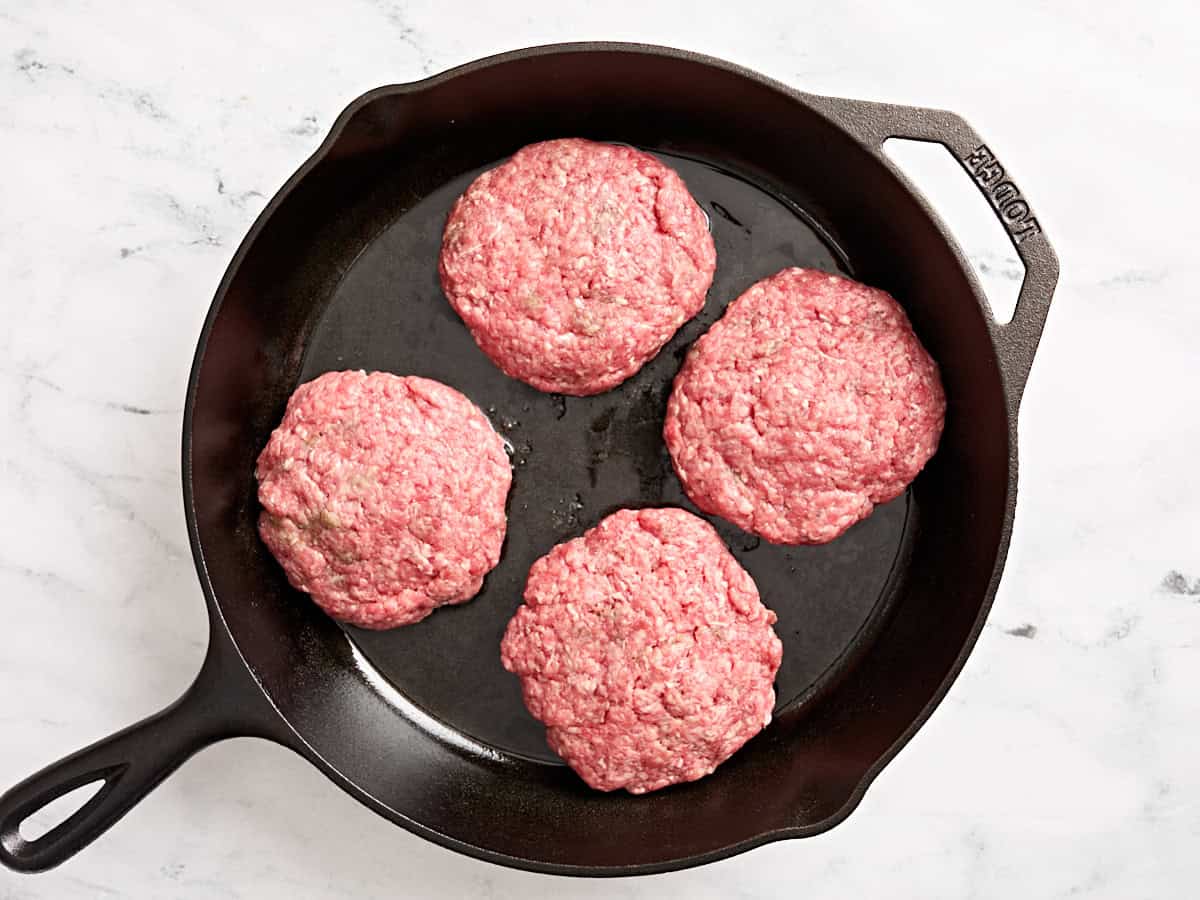 Juicy lucy patties cooking in a skillet.