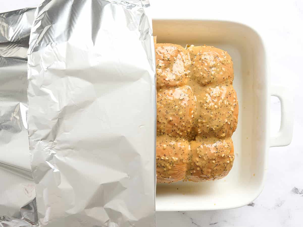 A baking dish of chicken sliders being covered with foil.