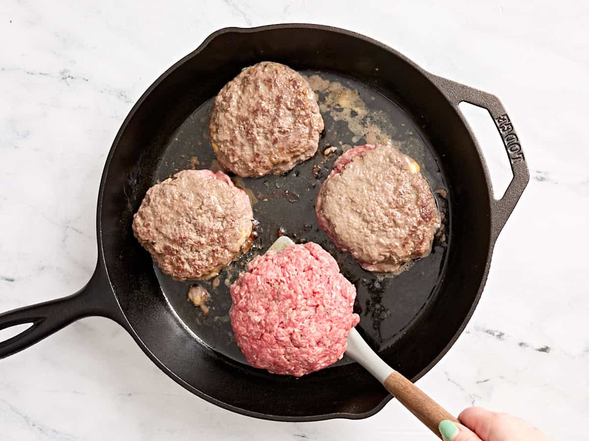 Juicy lucy patties being flipped with a spatula in a skillet.