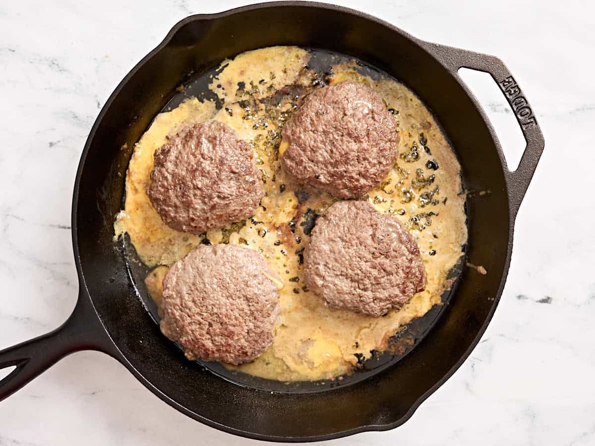 Juicy lucy patties cooking in a skillet.