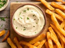 Overhead view of a bowl of homemade garlic aioli with fries.