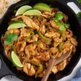 Overhead view of stovetop chicken fajita filling in a skillet with a wooden spoon.