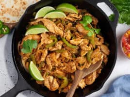 Overhead view of stovetop chicken fajita filling in a skillet with a wooden spoon.