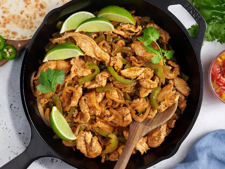 Overhead view of stovetop chicken fajita filling in a skillet with a wooden spoon.