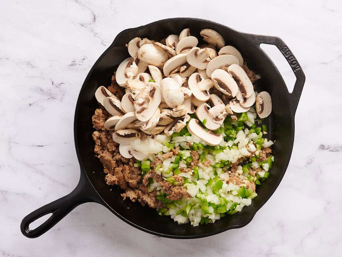 Sliced mushrooms, green bell pepper and onion in a skillet.