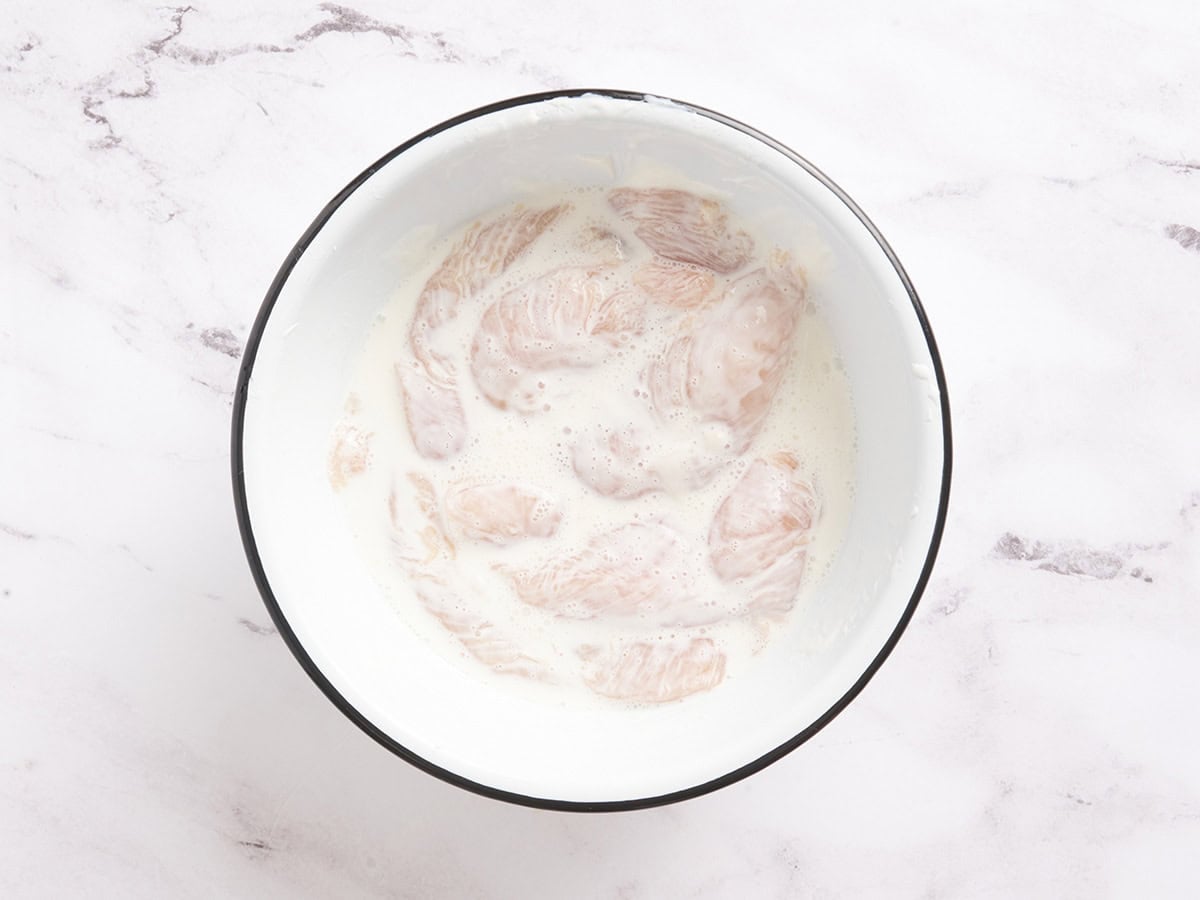 Chicken tenders in a bowl with yogurt and water.