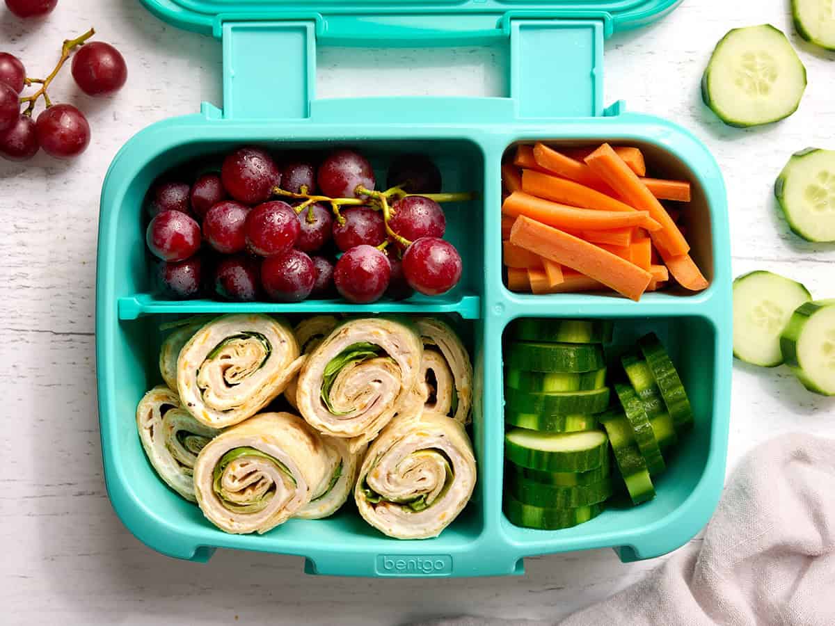 Overhead view of turkey pinwheel rollups, carrot sticks. cucumber slices, and grapes.