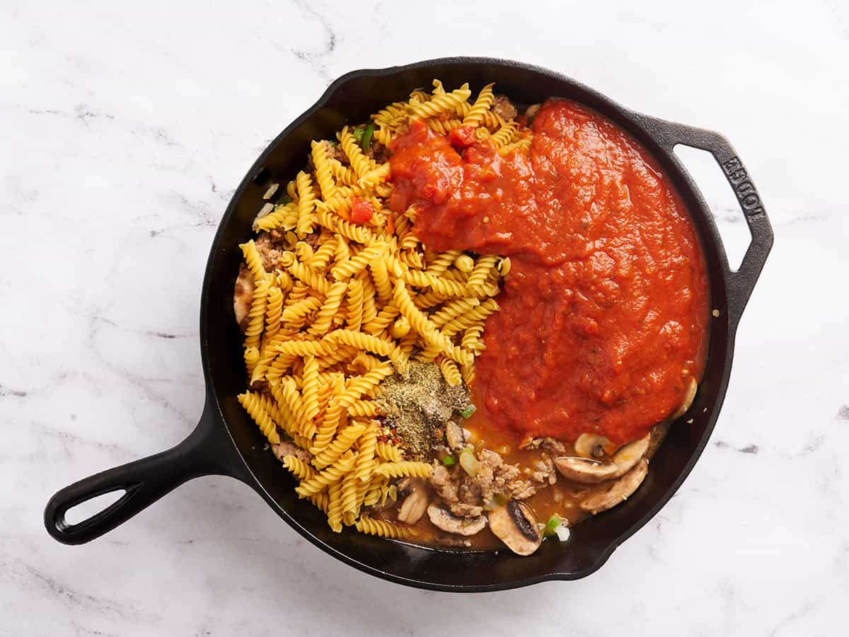 Pasta, sauce and mushrooms added to pizza casserole in a skillet.