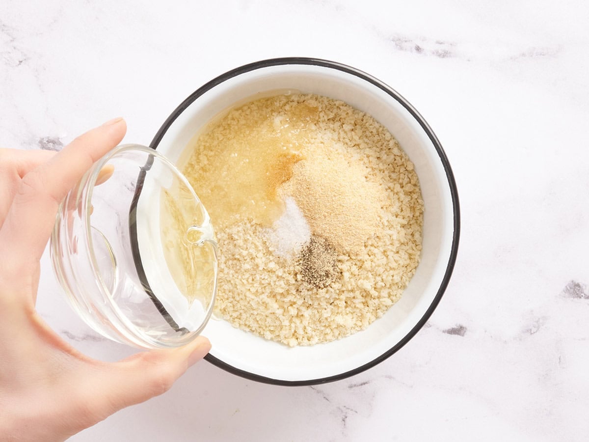 Oil being poured into a bowl of breadcrumbs and seasonings.