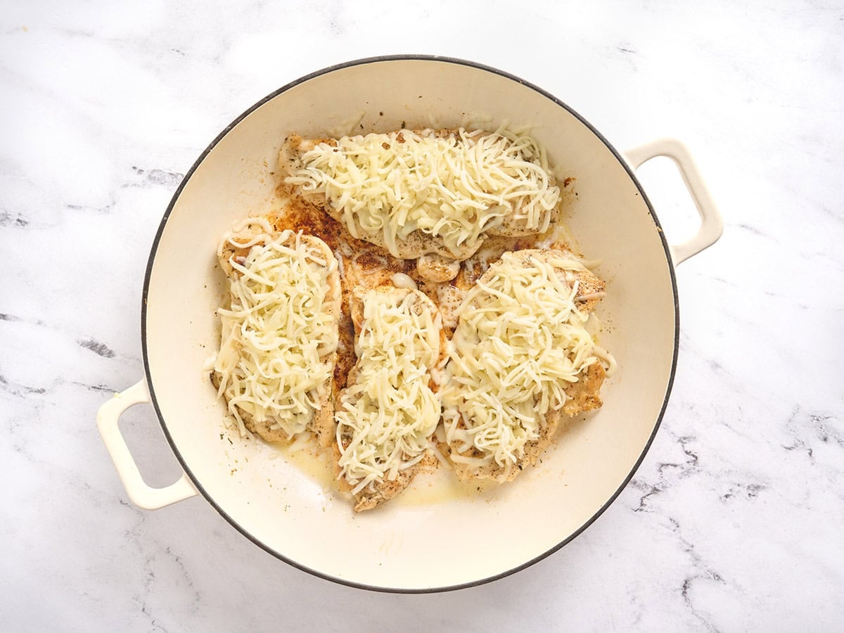 Chicken culets topped with mozzarella in a skillet.