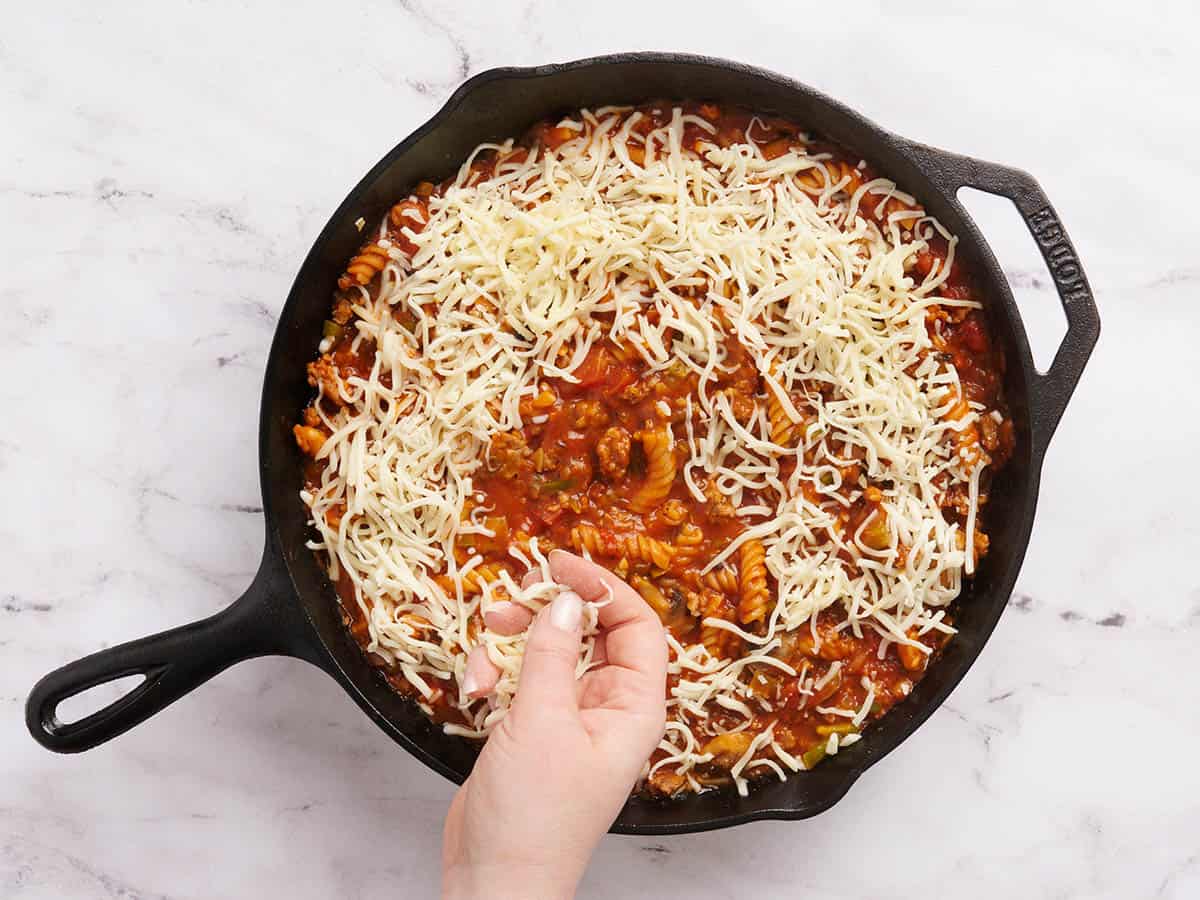 A hand sprinkling cheese over a pizza casserole in a skillet.