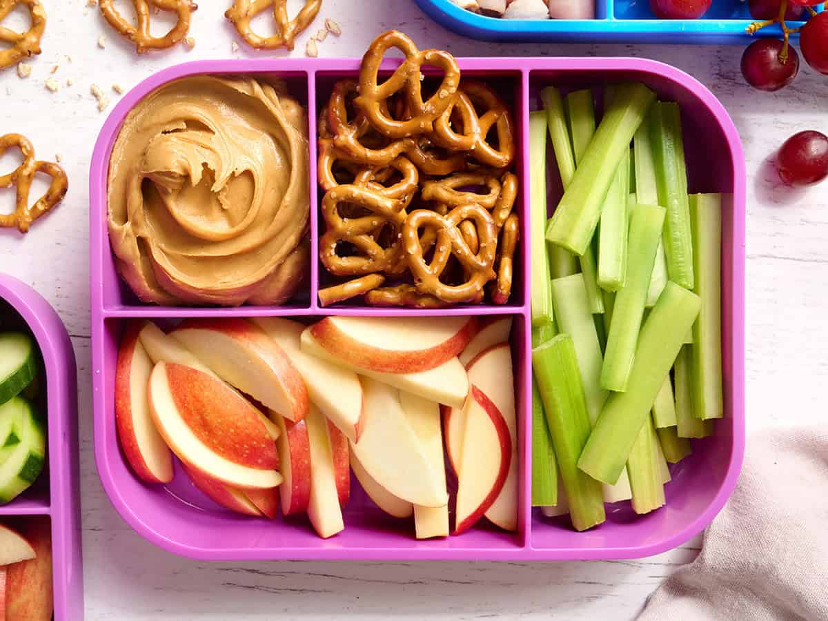 Overhead view of a peanut butter lunchbox with celery sticks, pretzels, apple slices, and peanut butter.