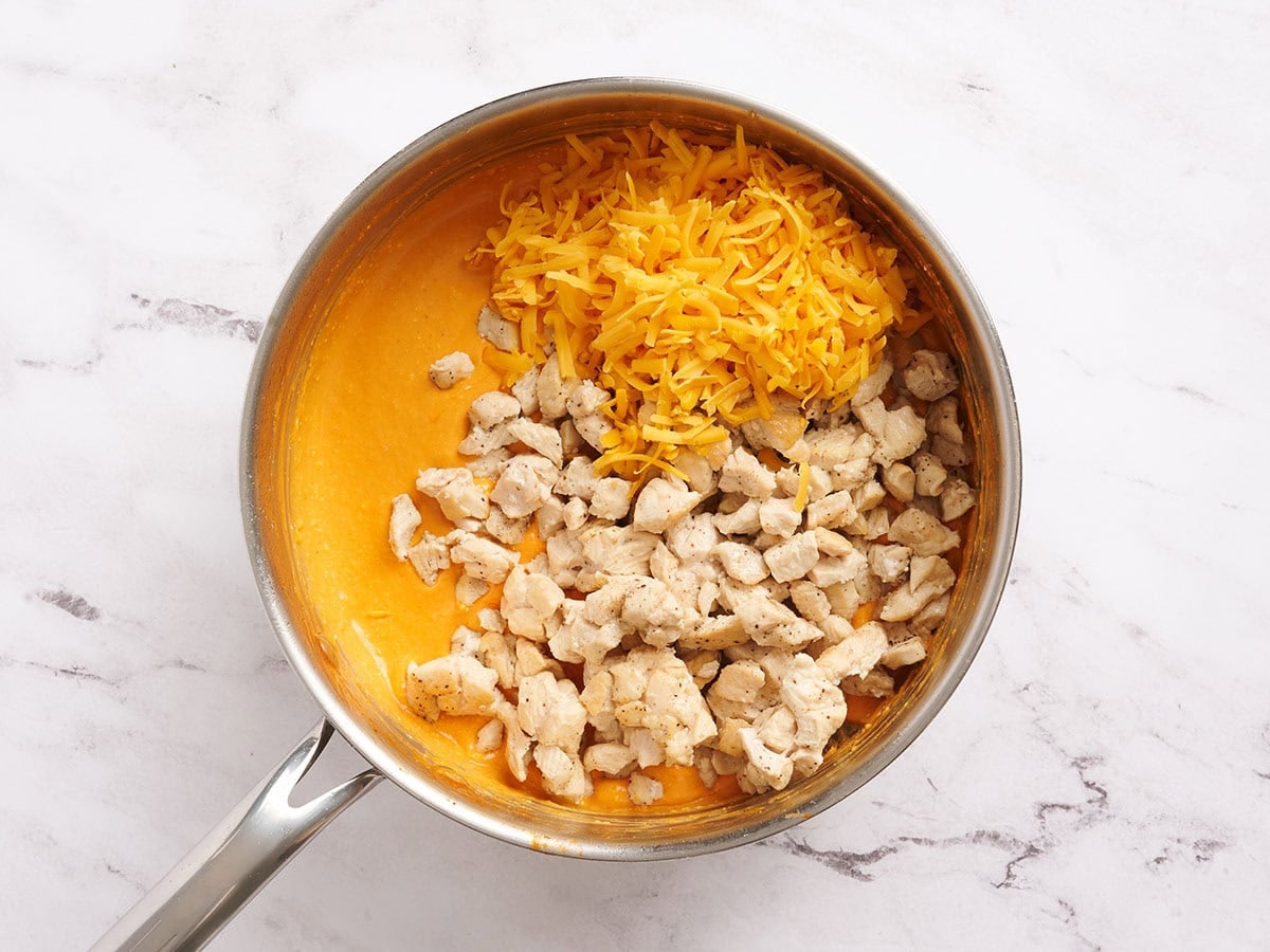 Cooked chicken, shredded cheese and buffalo sauce in a saucepan.
