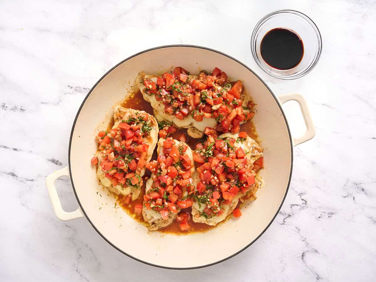 Chicken cutlets in a skillet topped with bruschetta.
