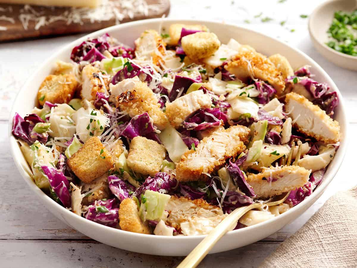 Side view of Casesar slaw with crispy chicken in a bowl with a fork.