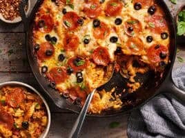 Overhead view of a skillet pizza casserole in a skillet next to a bowl.