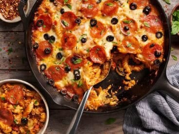 Overhead view of a skillet pizza casserole in a skillet next to a bowl.