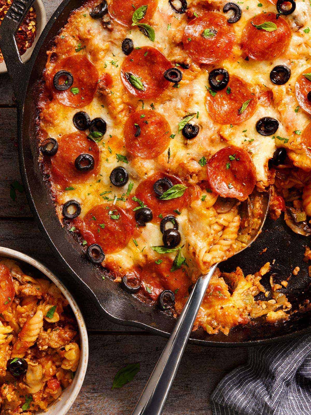 Overhead view of a skillet pizza casserole in a skillet next to a bowl.