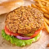 Overhead side view of a lentil burger in a hamburger bun, with salad and the top bun removed.