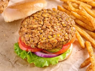 Overhead side view of a lentil burger in a hamburger bun, with salad and the top bun removed.