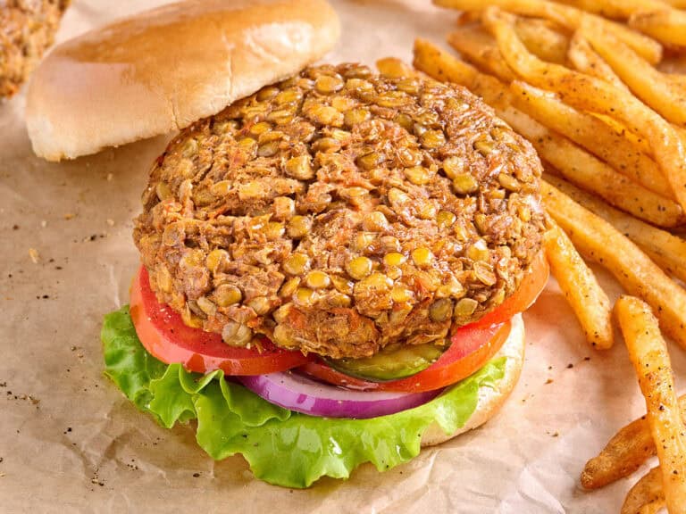 Overhead side view of a lentil burger in a hamburger bun, with salad and the top bun removed.
