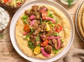 Overhead view of a sheet pan doner kebab on a pita bead with salad and tzatziki sauce.