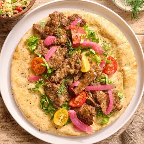 Overhead view of a sheet pan doner kebab on a pita bead with salad and tzatziki sauce.
