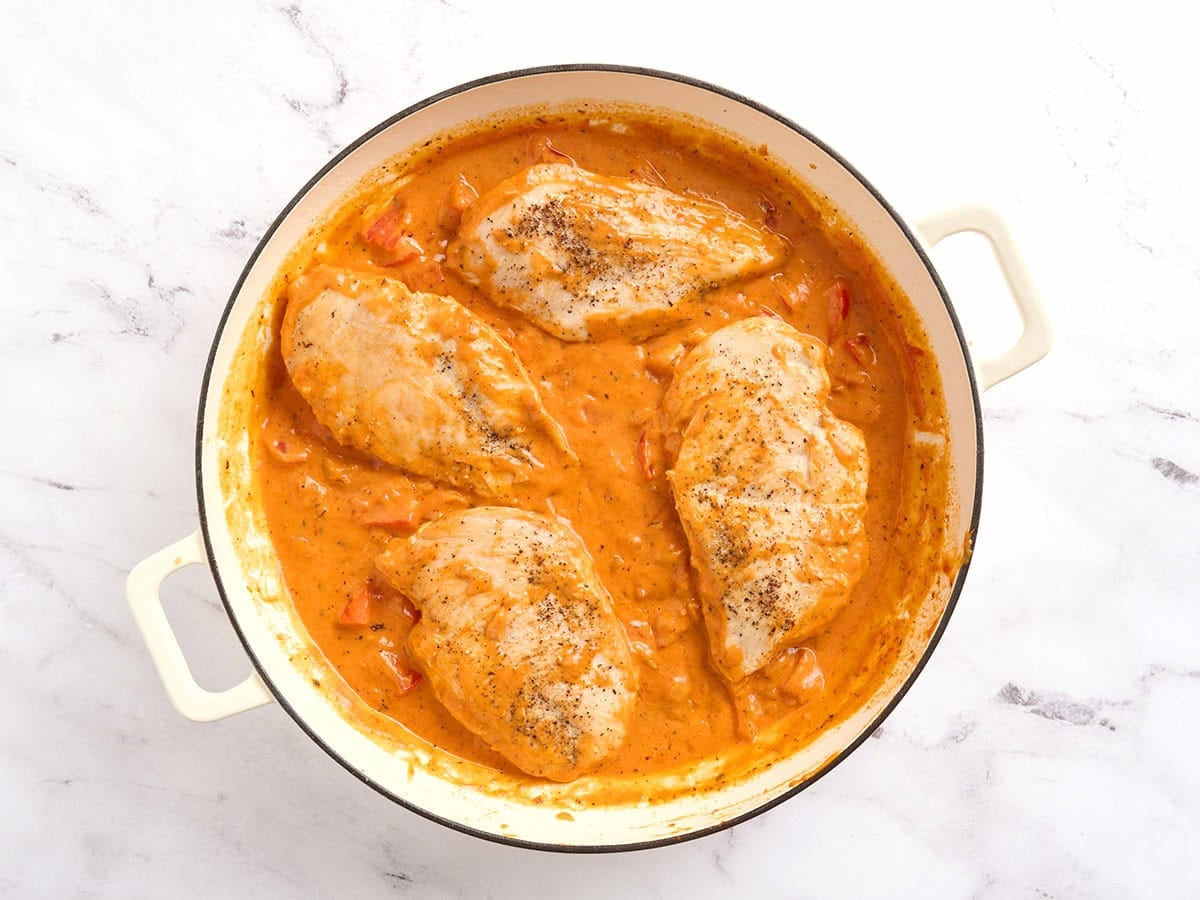 Chicken added to a skillet of creamy tomato sauce.