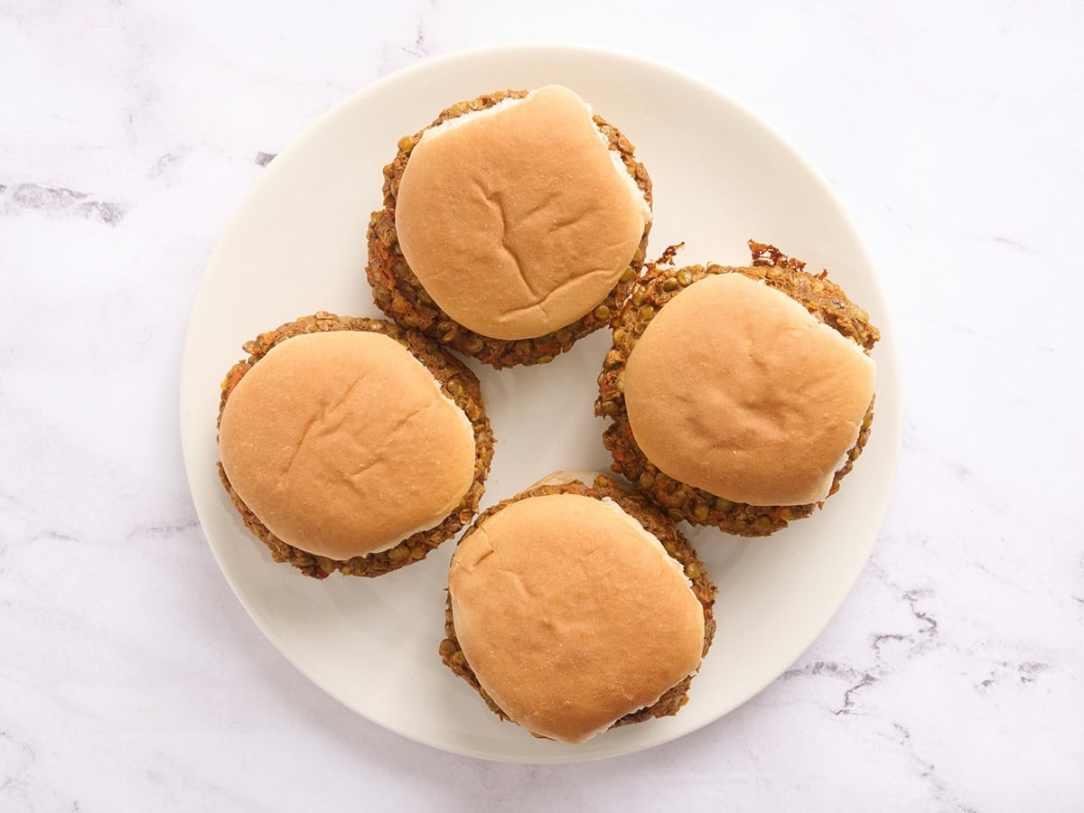 Overhead view of four lentil burgers in hamburger buns on a plate.