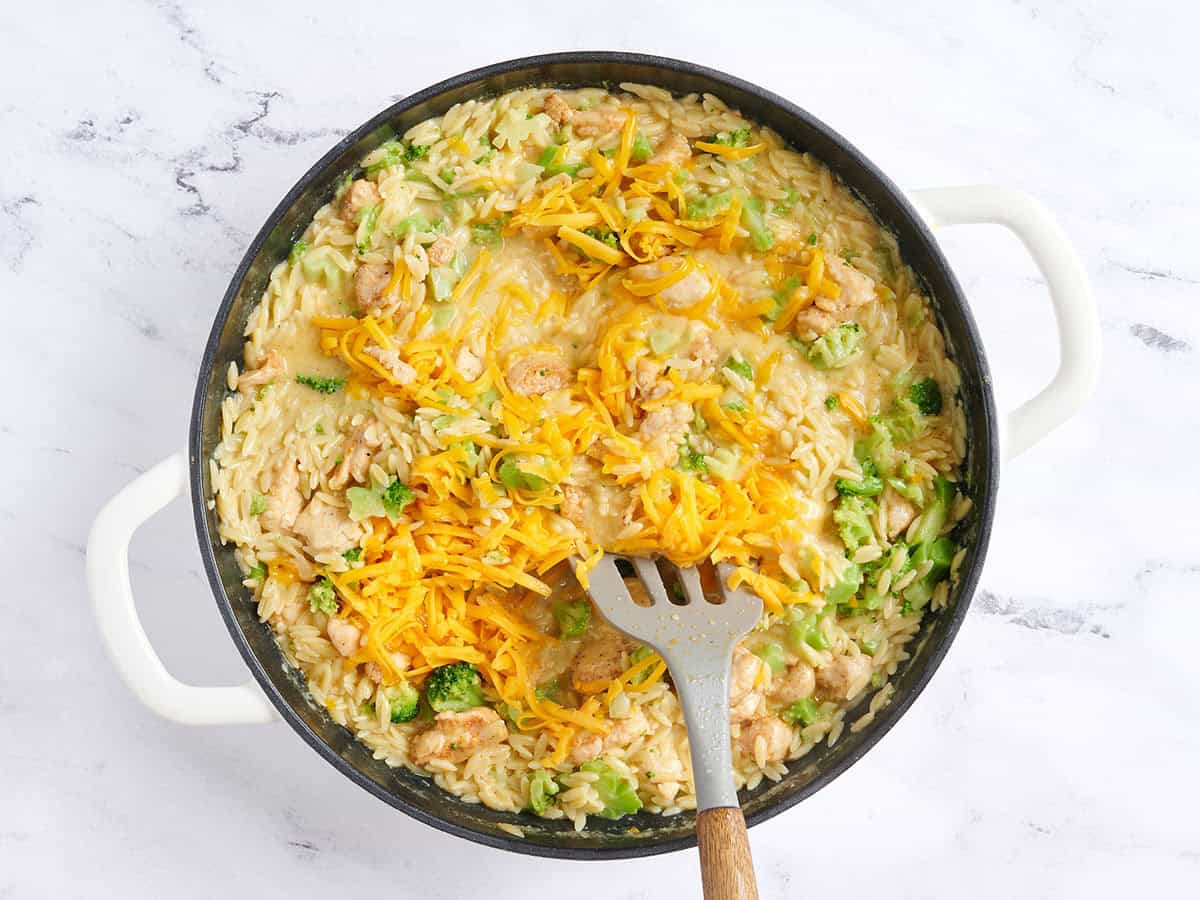 Shredded cheddar being stirred into a pot of chicken broccoli casserole.