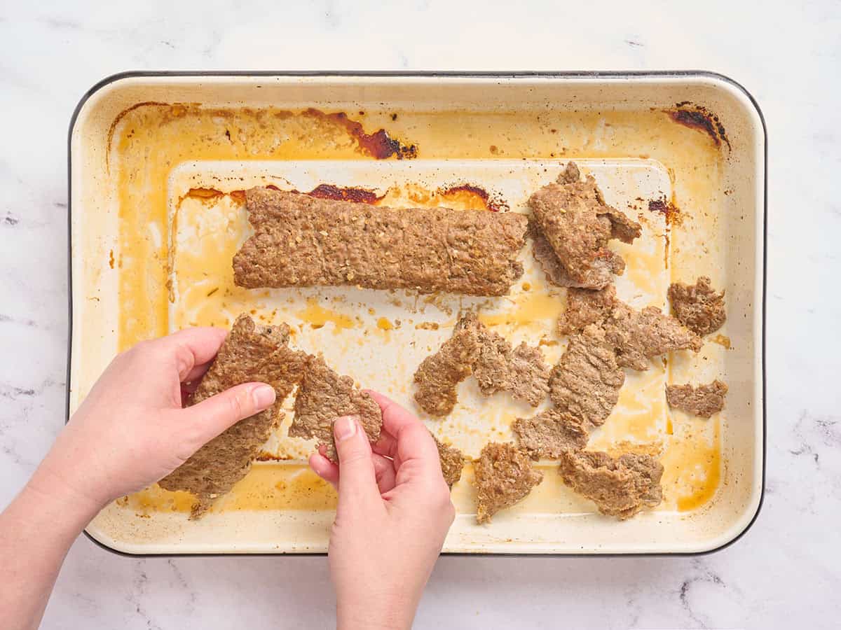 Hands shredding sheet pan donner kebab meat into smaller pieces.