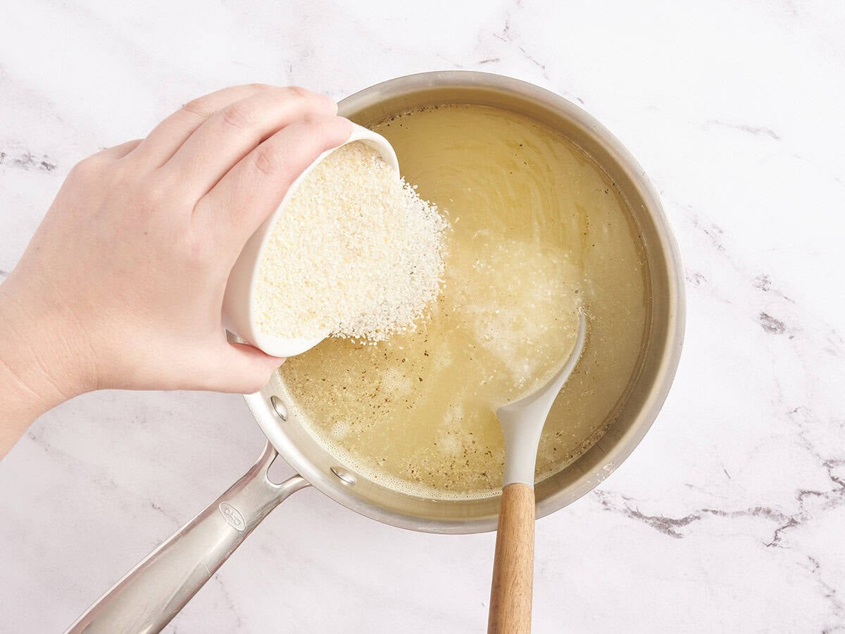 Grits being poured into water and chicken broth in a pan.