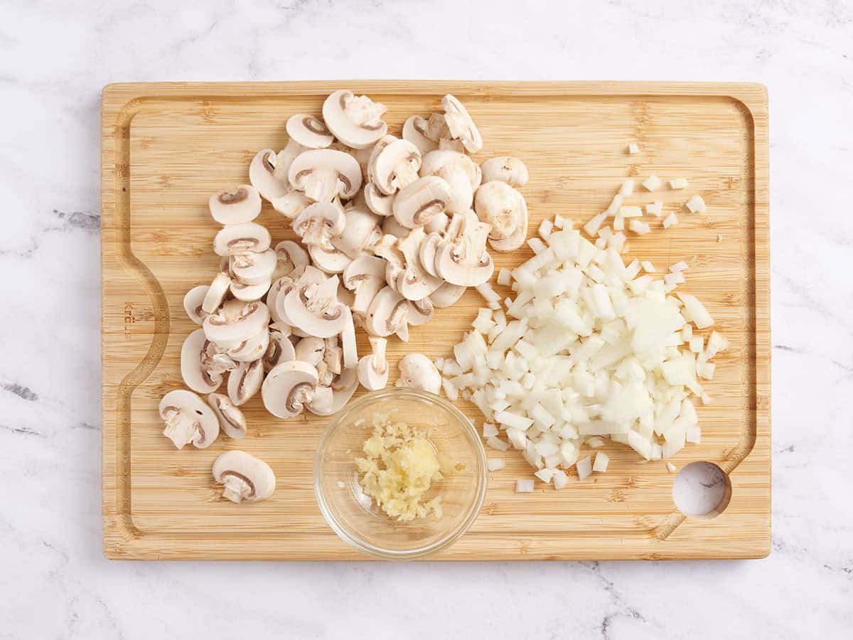 Sliced mushrooms, diced onion and minced garlic on a cutting board.